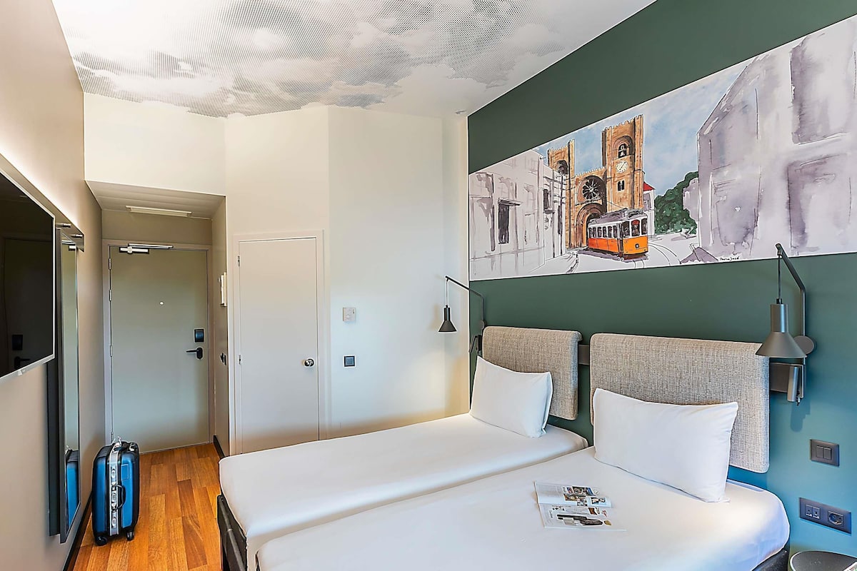 Une chambre d’hôtel avec un lit, un téléviseur à écran plat, un tableau, une lampe et une valise.