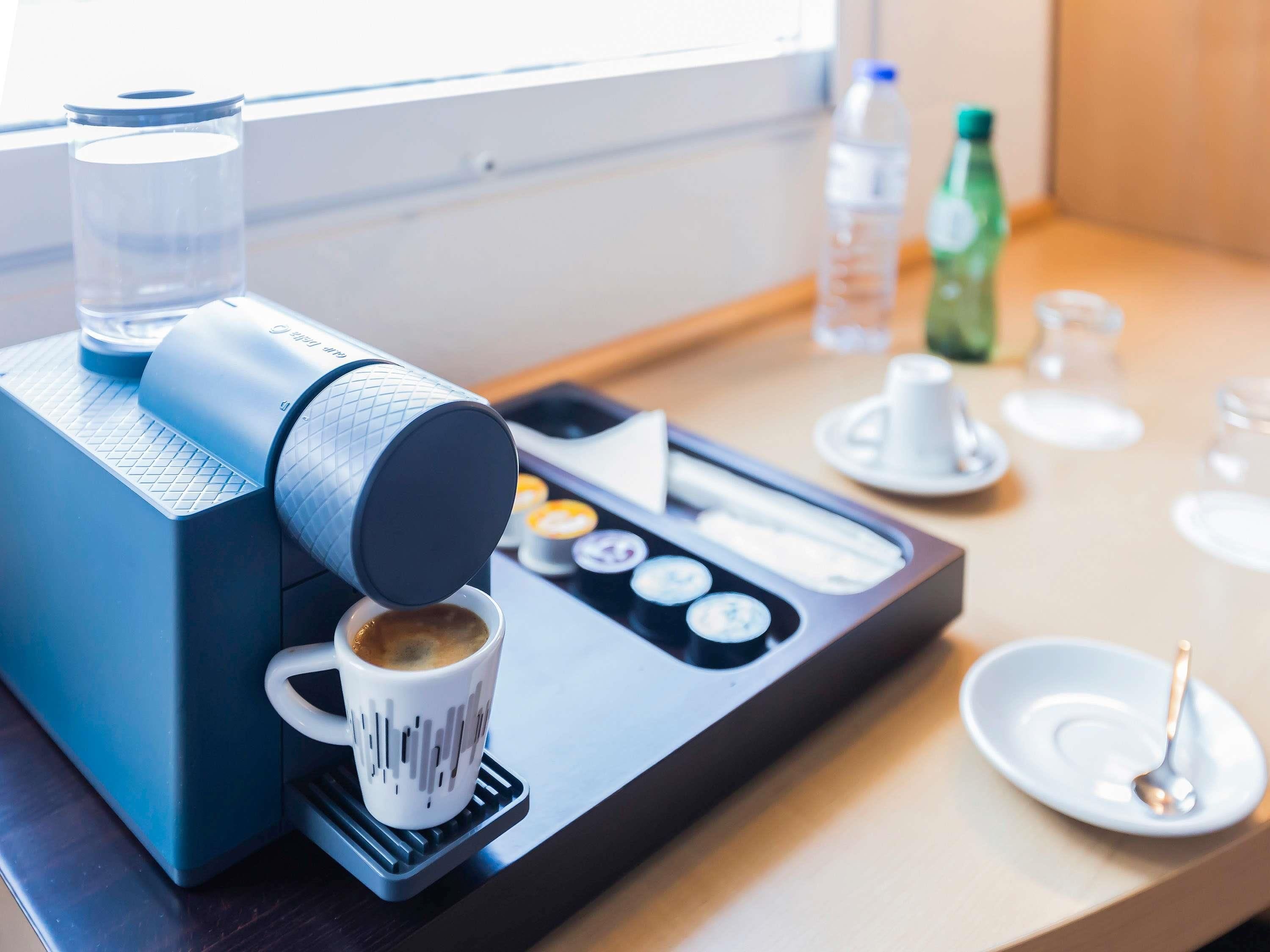A coffee machine dispensing coffee into a cup, a water bottle, and a glass on a table.