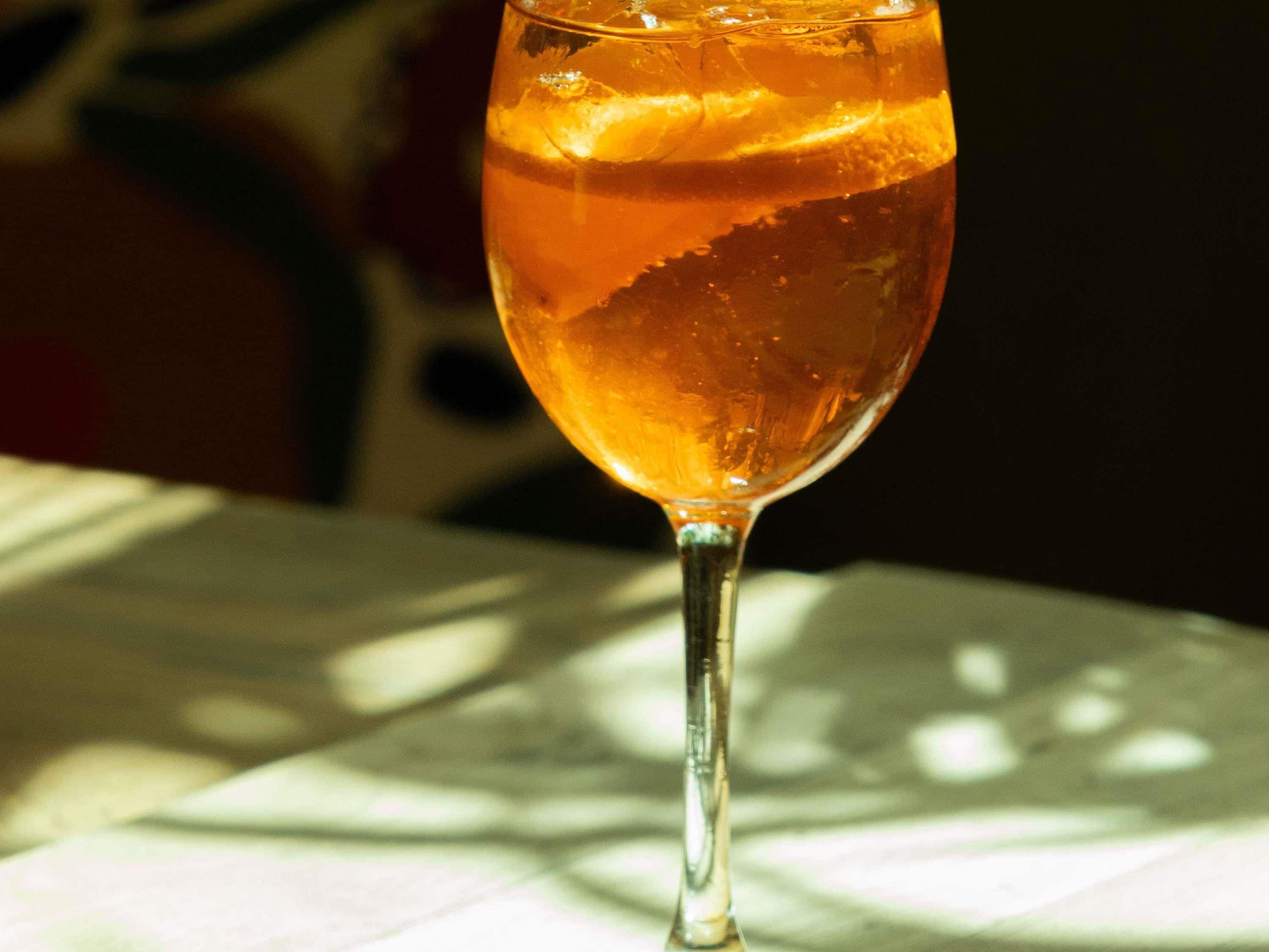 Een glas amberkleurige vloeistof met ijsblokjes, op een tafel met een decoratieve tafelkleed.