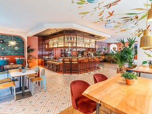 A bar area with a counter, stools, and a variety of bottles and glasses. There are tables and chairs around the bar, and the floor has a patterned tile design. - ibis Lisboa Parque das Naçoes (Lisbon)