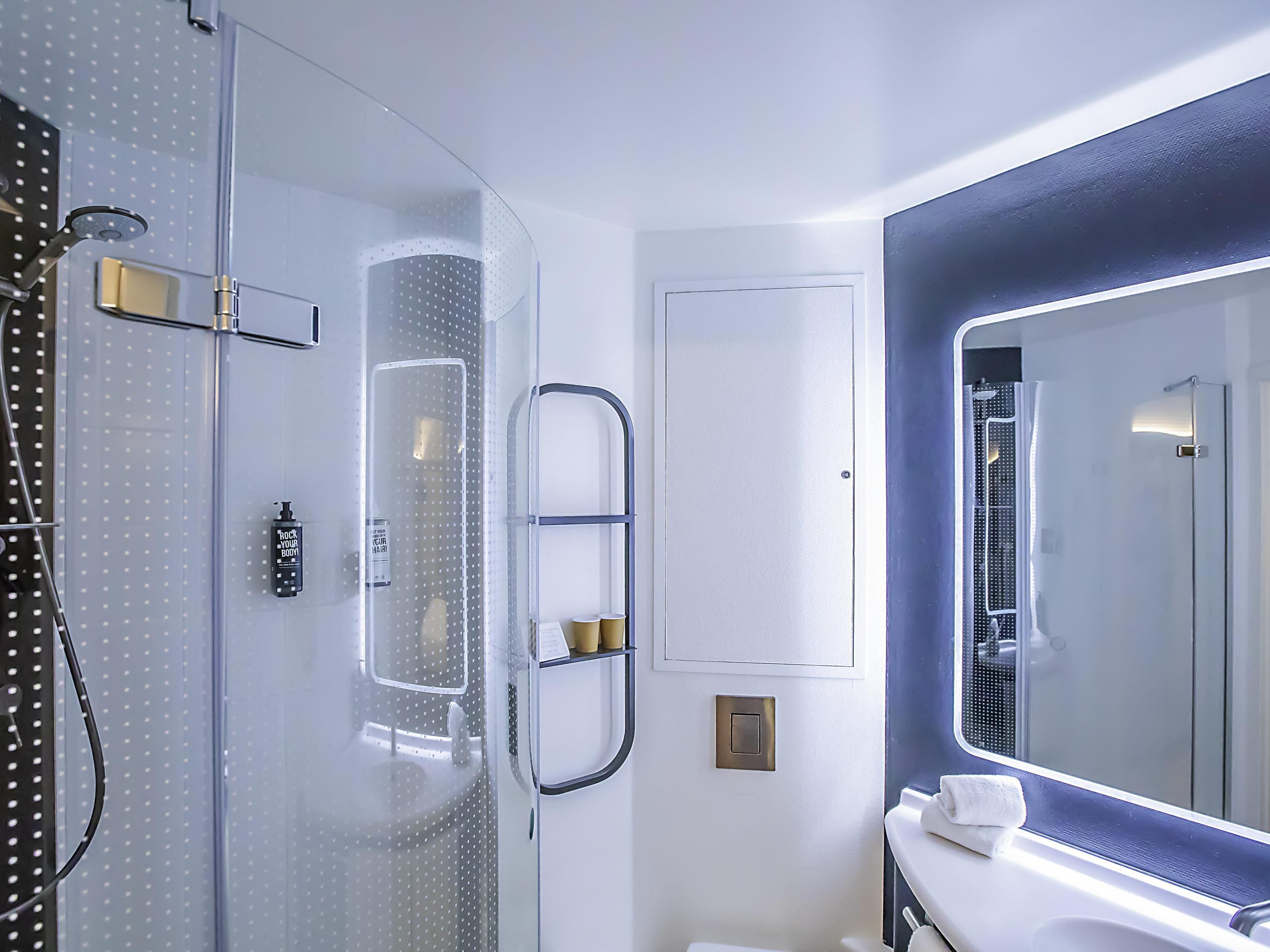 A modern bathroom with a glass shower enclosure, a large mirror, and a white vanity with a towel.