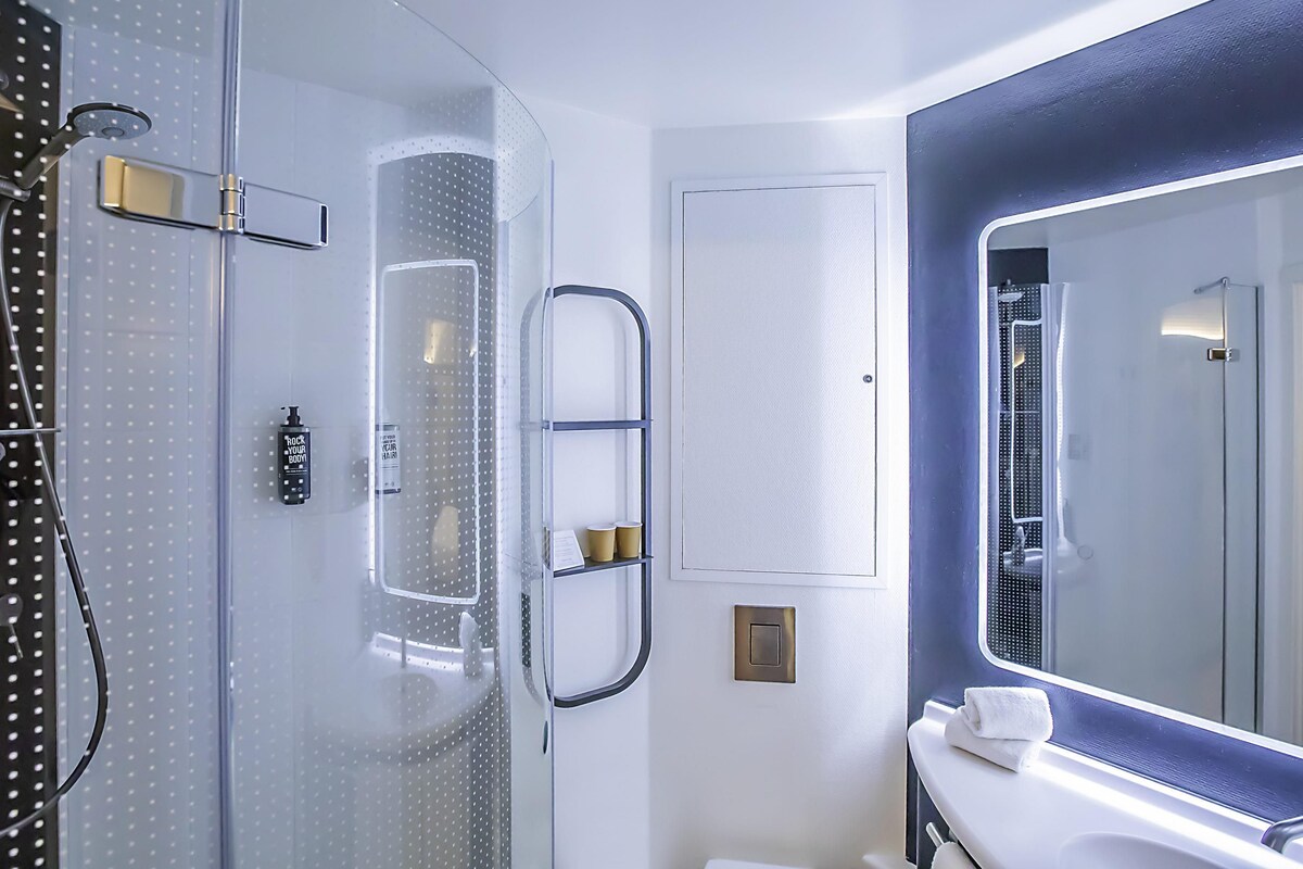 A modern bathroom with a glass shower enclosure, a large mirror, and a white vanity with a towel.