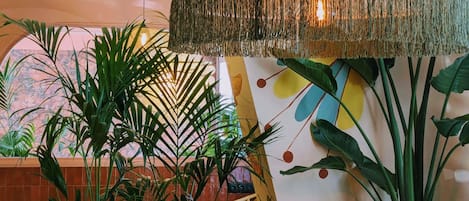 A room with a large hanging lamp, a wicker chair, and various potted plants.