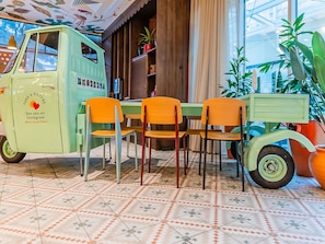 Een groene oldtimer vrachtwagen met een tafel en stoelen in een kamer met een vloer van versierde tegels en potplanten.