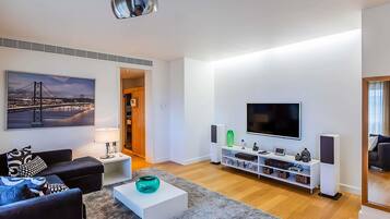 Un salon moderne comprenant un canapé, une table basse, un téléviseur et un tableau représentant un pont.
