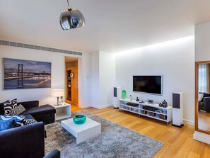 Un salon moderne comprenant un canapé, une table basse, un téléviseur et un tableau représentant un pont.