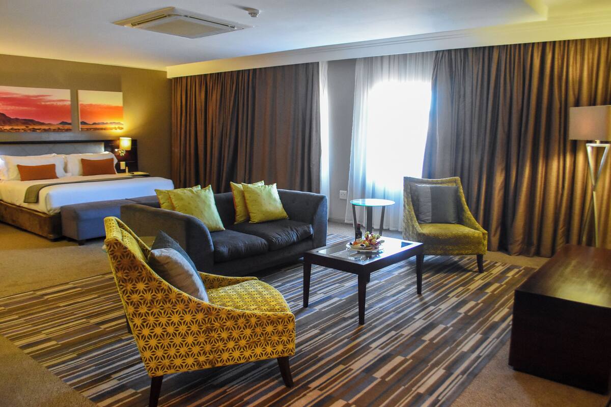A hotel room with a bed, a sofa, two armchairs, a coffee table, and a lamp.
