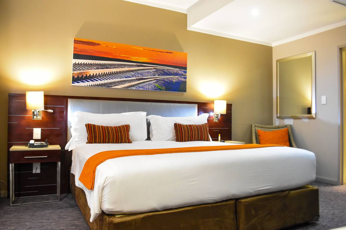 A hotel room with a large bed, two bedside tables, a headboard, and a painting above the bed.