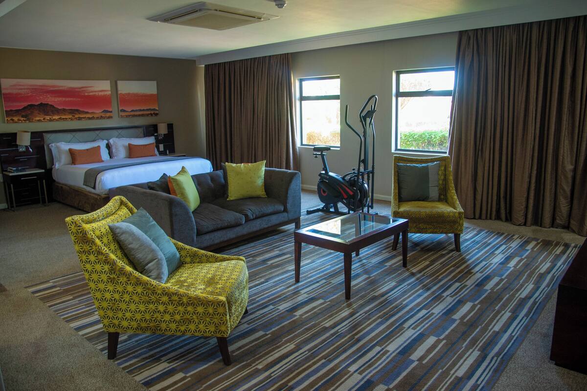 A hotel room with a bed, a sofa, two armchairs, a coffee table, and a window with curtains.