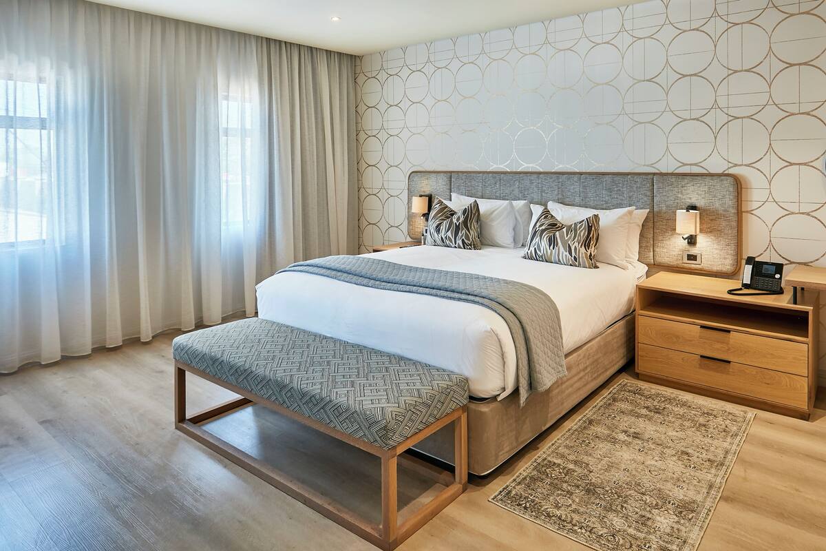 A modern bedroom with a large bed, bedside tables, a bench, and a patterned rug.