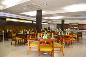 A spacious restaurant with multiple tables and chairs, air conditioning vents, and a tiled floor.