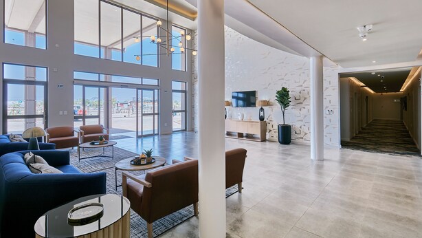 A spacious lobby with a blue sofa, brown armchairs, a coffee table, and a reception desk.
