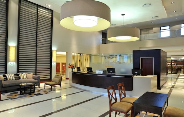 A modern hotel lobby with a reception desk, seating area, and a glass partition.