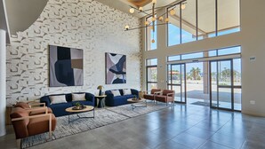 A spacious lobby with a modern design, featuring a blue sofa, brown armchairs, and abstract art on the walls.