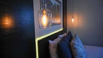 A bedroom with a bed, pillows, a framed picture, and two pendant lights.