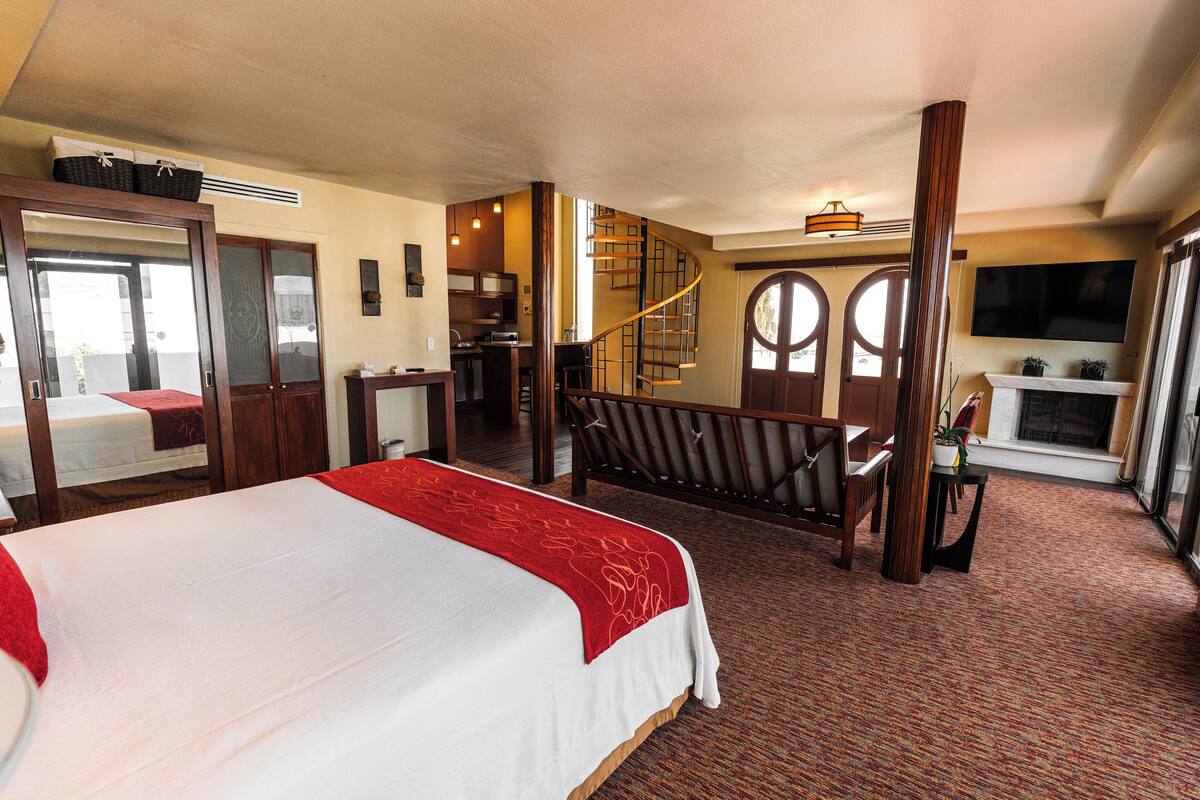 A hotel room with a large bed, a desk, a chair, a staircase, and a TV.