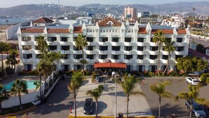 A multi-story hotel with a central courtyard, palm trees, and a swimming pool. - Corona Hotel & Spa (Ensenada)