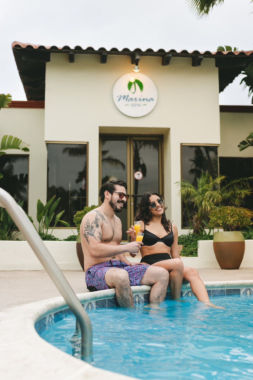 A couple sitting by a pool with a sign reading "Marina SPA" above.