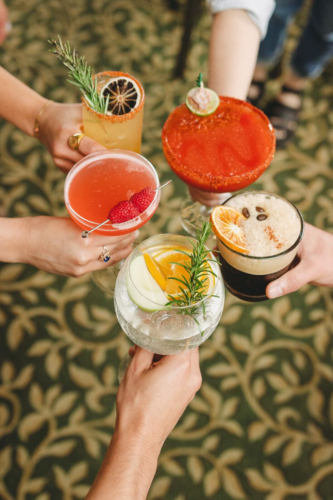 A group of people holding various cocktails, each garnished with different fruits and herbs.