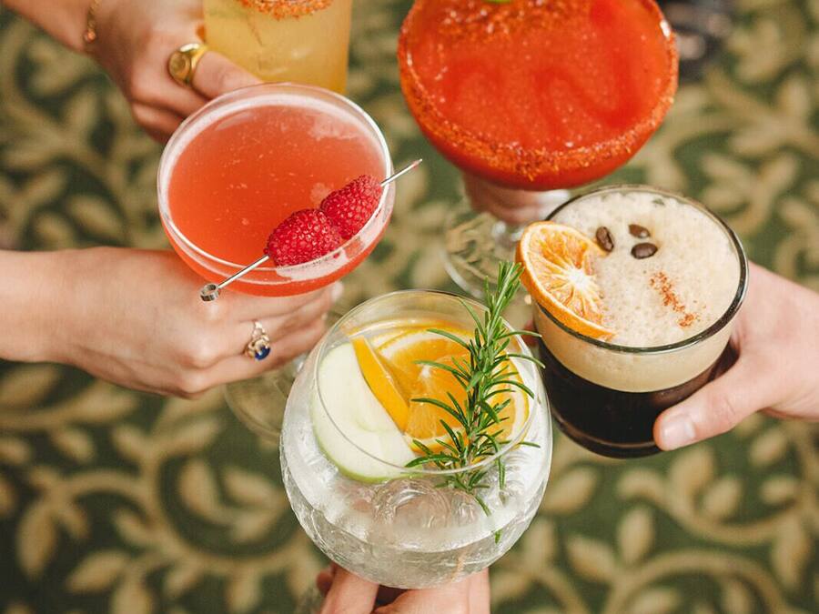 A group of people holding various cocktails, each garnished with different fruits and herbs.
