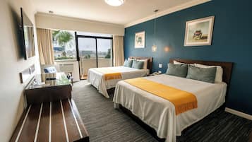 A hotel room with two beds, a desk, and a large window with a view.