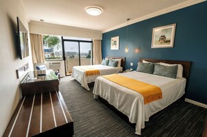 A hotel room with two beds, a desk, and a large window with a view.