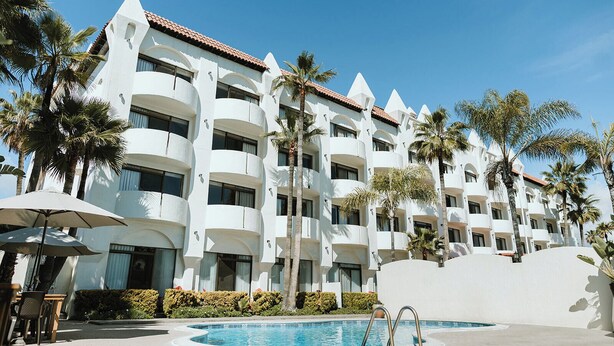 A multi-story hotel with balconies, a swimming pool, and palm trees. - Corona Hotel & Spa (Ensenada)