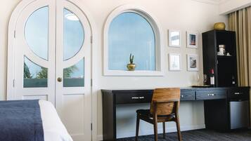 Quarto de hotel com cama, escrivaninha, cadeira, janela e minibar.