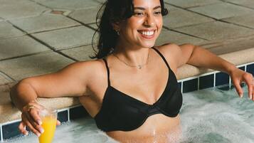 A person in a black bikini in a hot tub with a glass of orange juice.