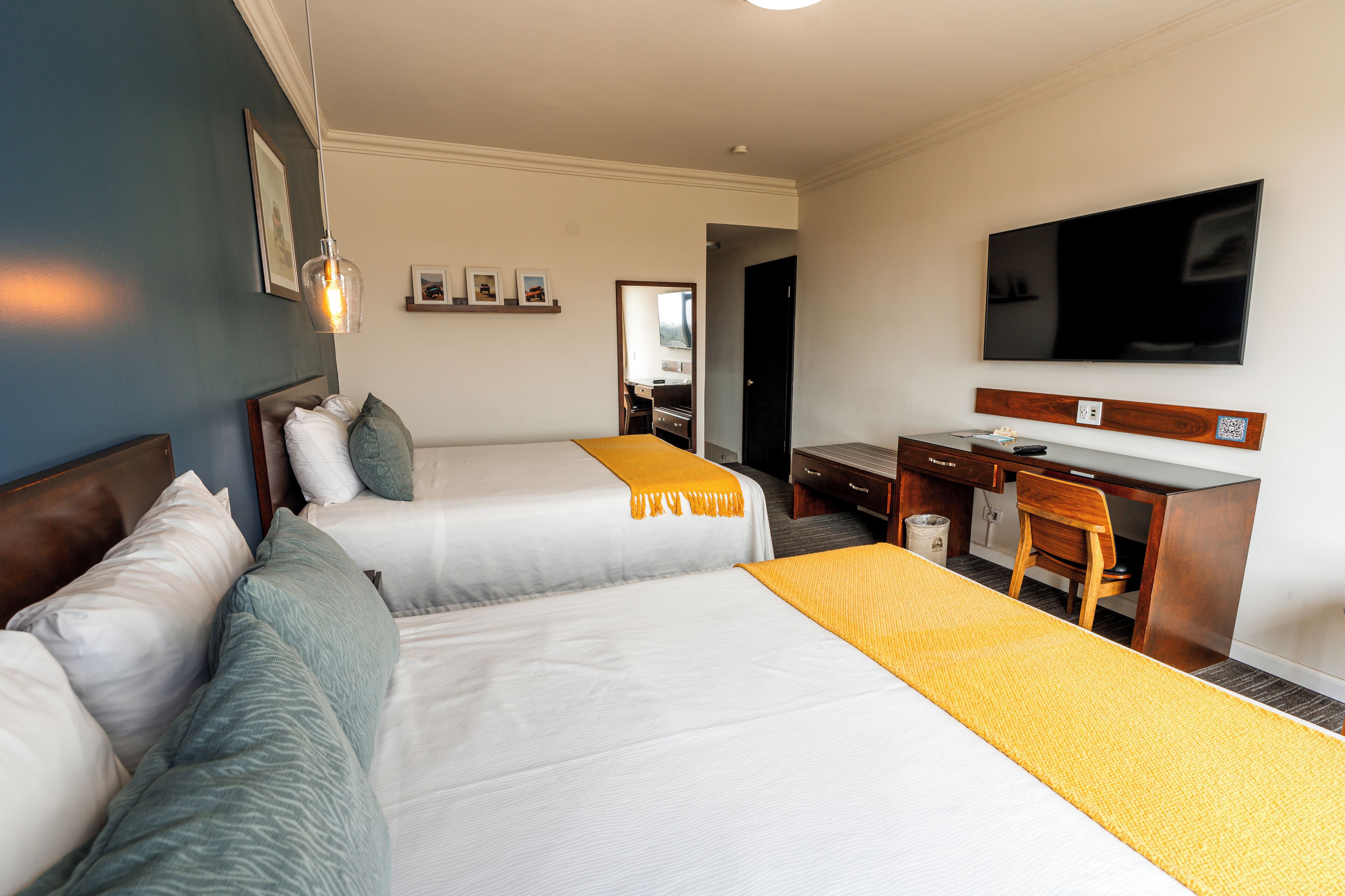 A hotel room with two beds, a desk, a chair, a TV, and a bathroom visible through an open door.
