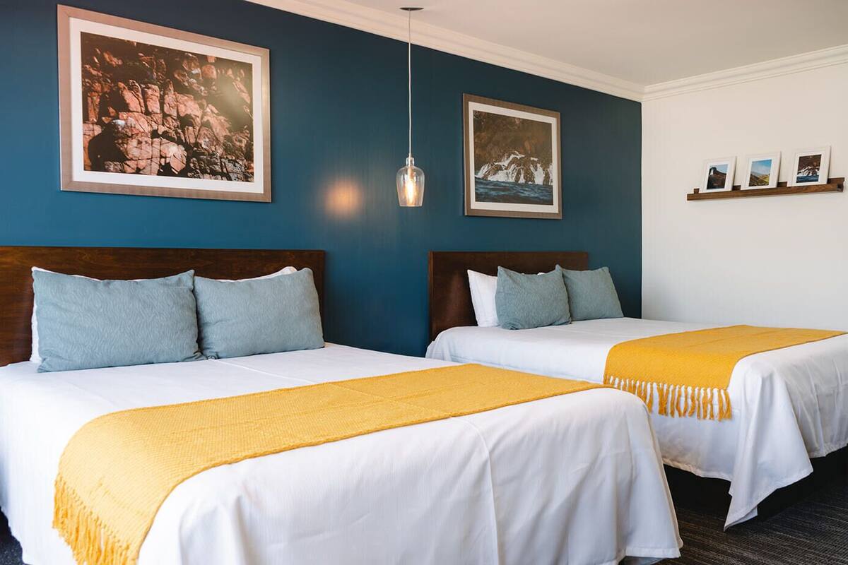 A hotel room with two beds, each with white linens and a yellow throw blanket. There are framed pictures on the wall and a pendant light above the beds.