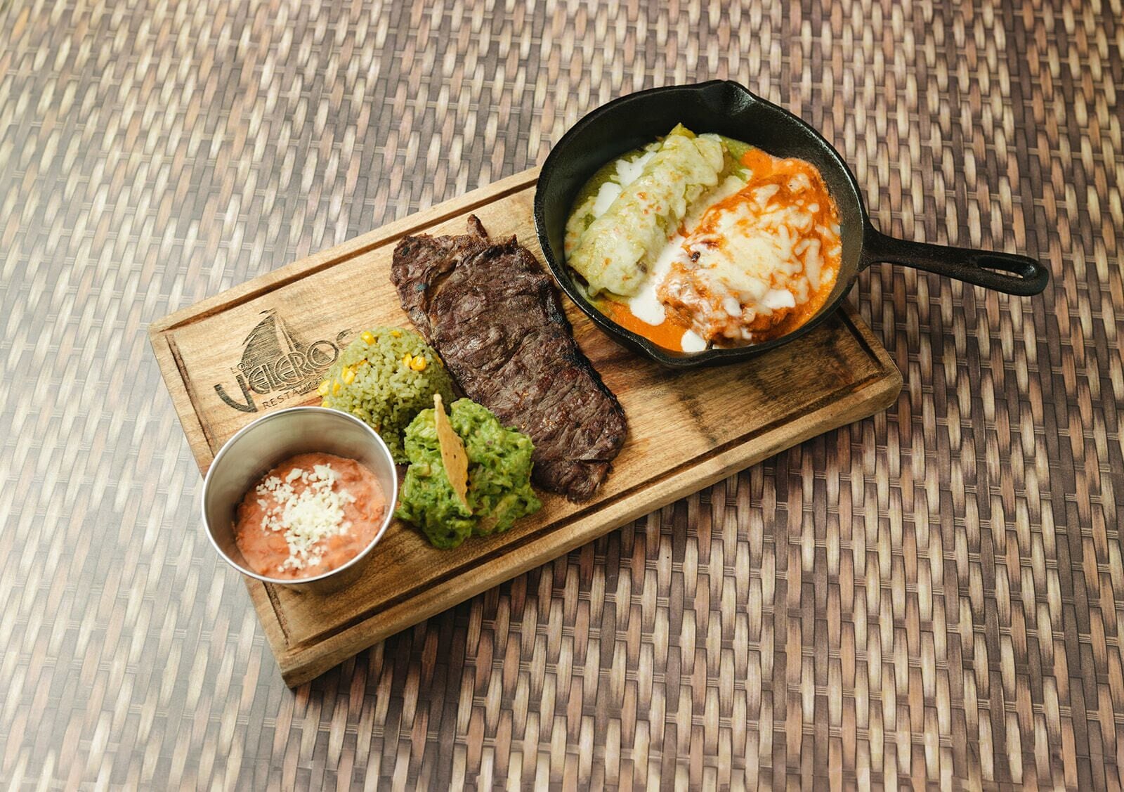 A wooden serving board with a steak, guacamole, rice, and a bowl of salsa.