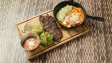 A wooden serving board with a steak, guacamole, rice, and a bowl of salsa.