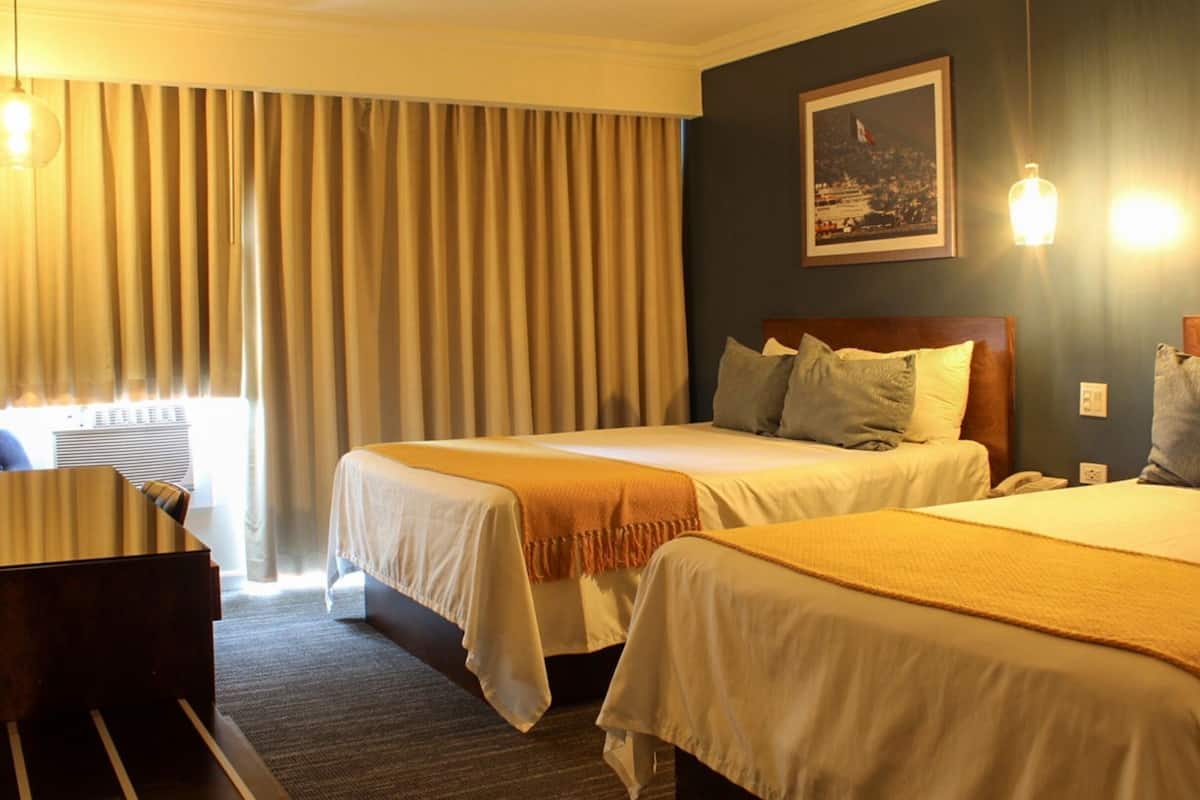 A hotel room with two beds, a desk, and a window with curtains.