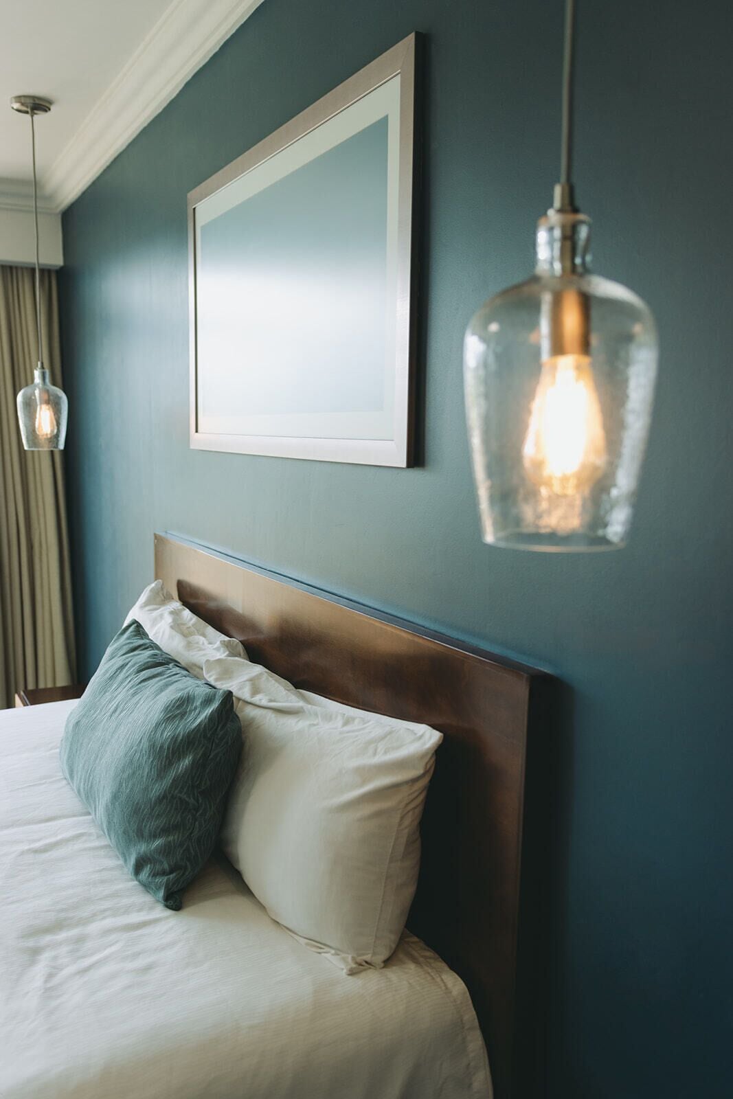 Una cama bien hecha con cabecera de madera, un cuadro en la pared y una lámpara colgante.