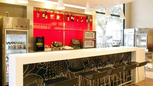 A bar area with a red backdrop, a refrigerator, a microwave, and bar stools. - ibis BH Afonso Pena Savassi (Belo Horizonte)