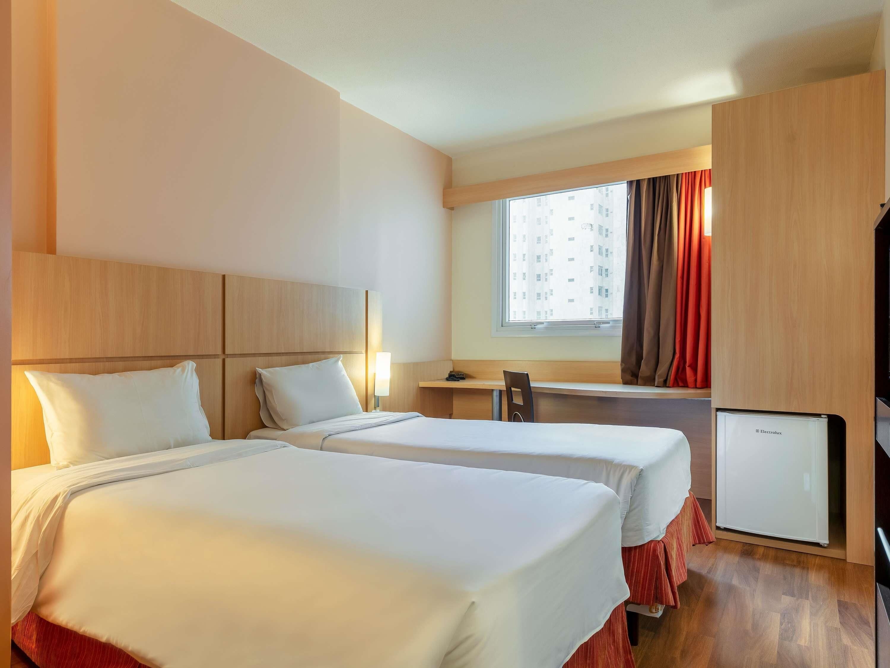 Habitación de hotel con dos camas, un escritorio, una silla, un televisor y una ventana con cortinas.