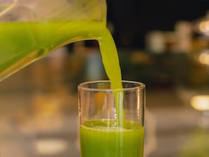 A clear glass being filled with a green liquid.