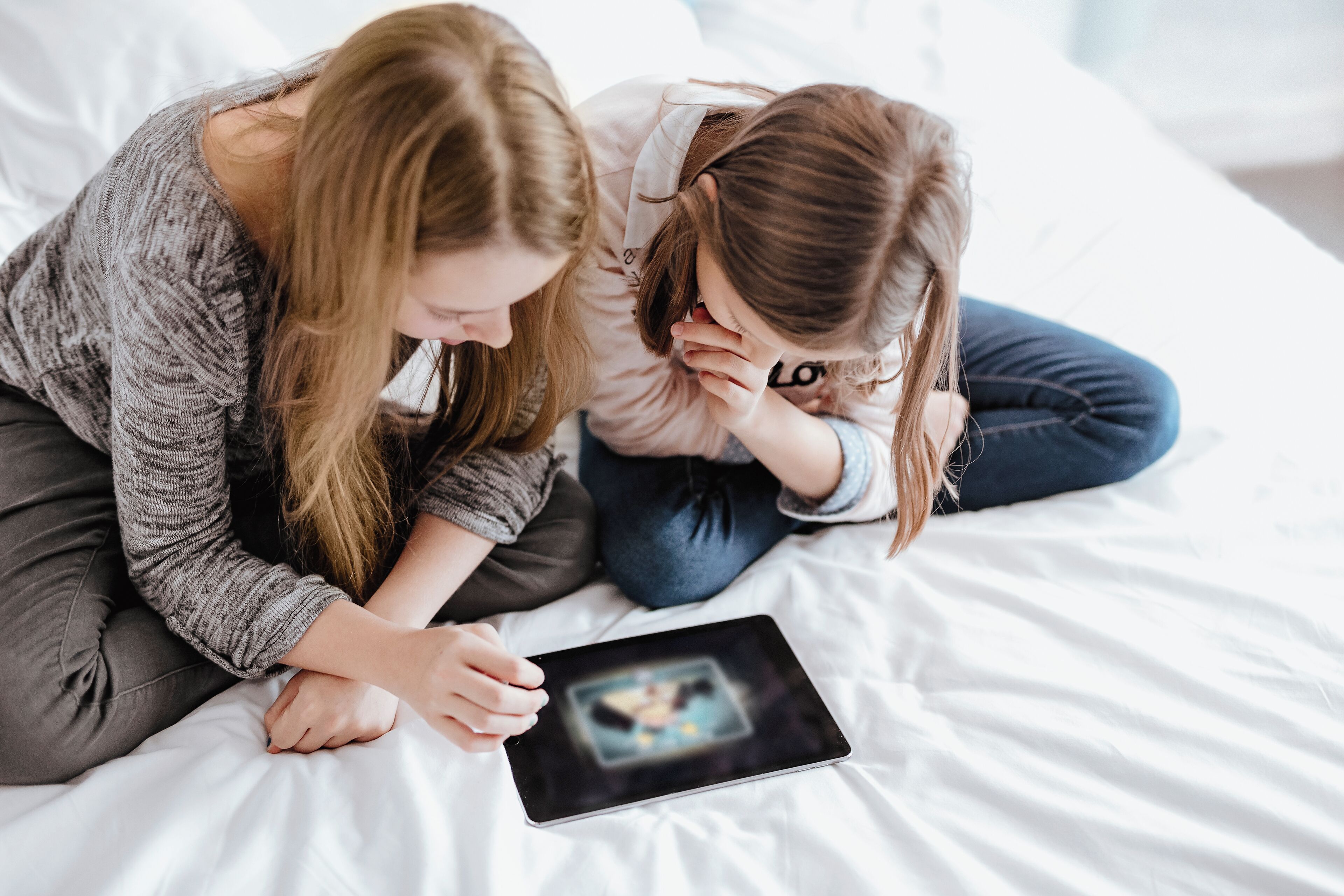 Deux personnes assises sur un lit, une tablette à la main.