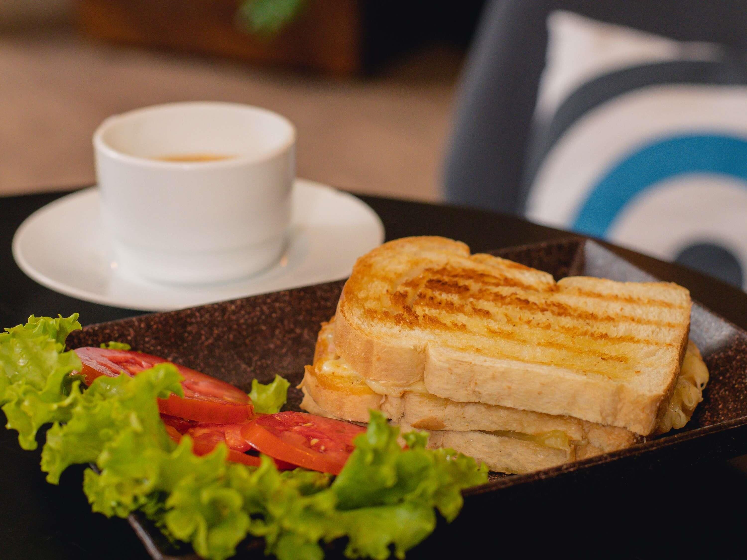 A sandwich on a plate with lettuce and tomato, and a cup of coffee on a saucer.