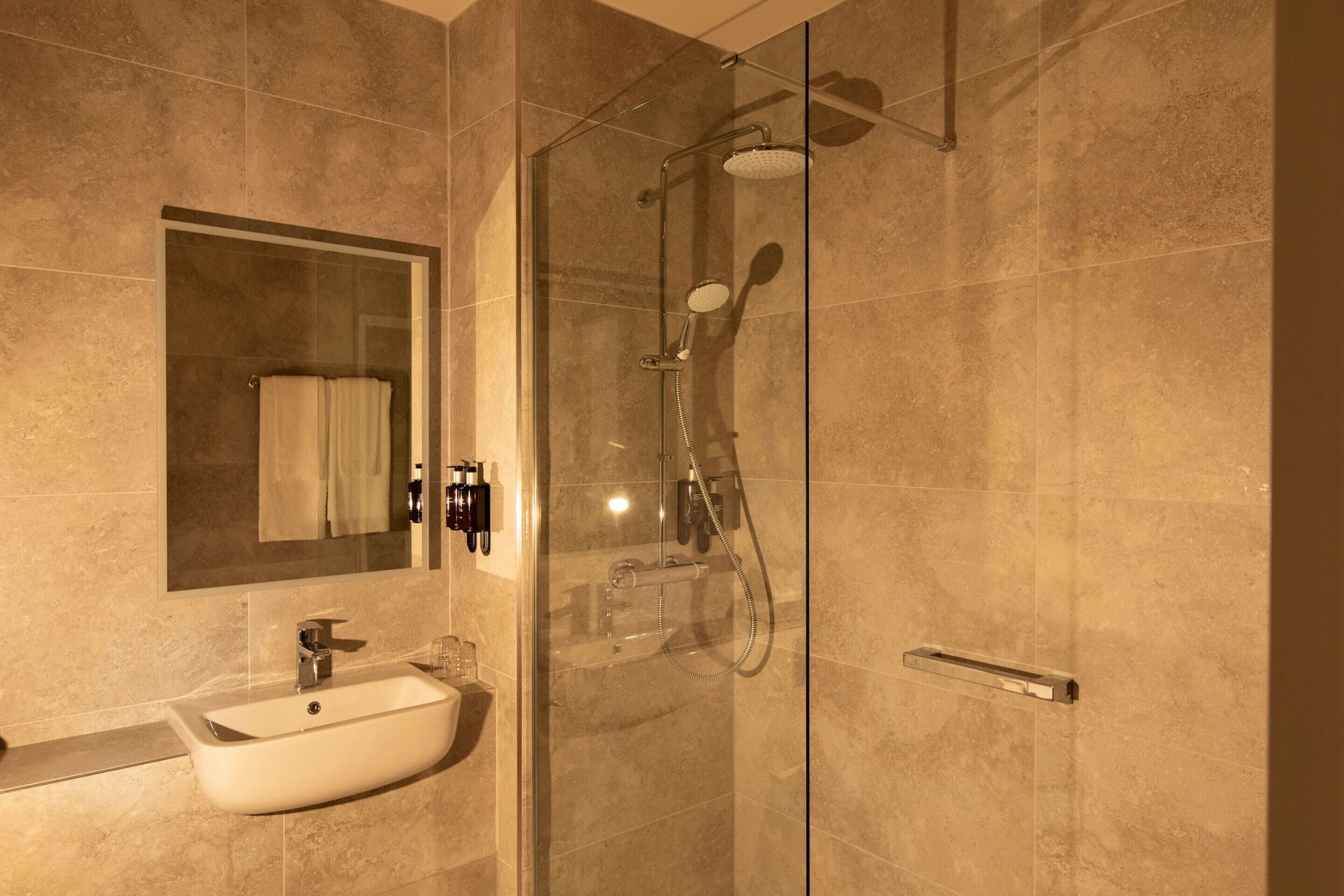 A modern bathroom with a glass-enclosed shower, a white sink, and a large mirror.
