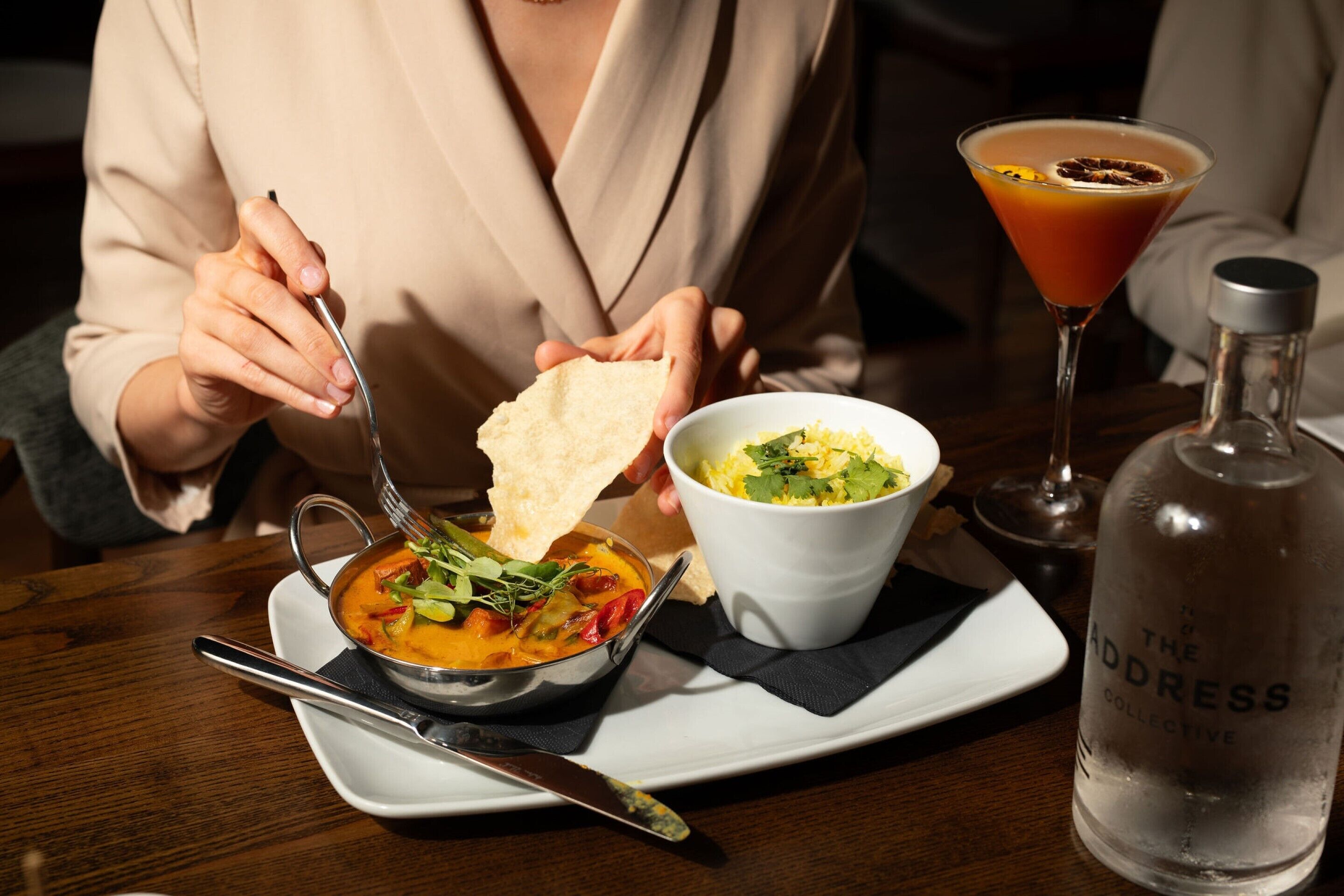 A person dining at a table with a bowl of soup, a plate of flatbread, and a cocktail glass.