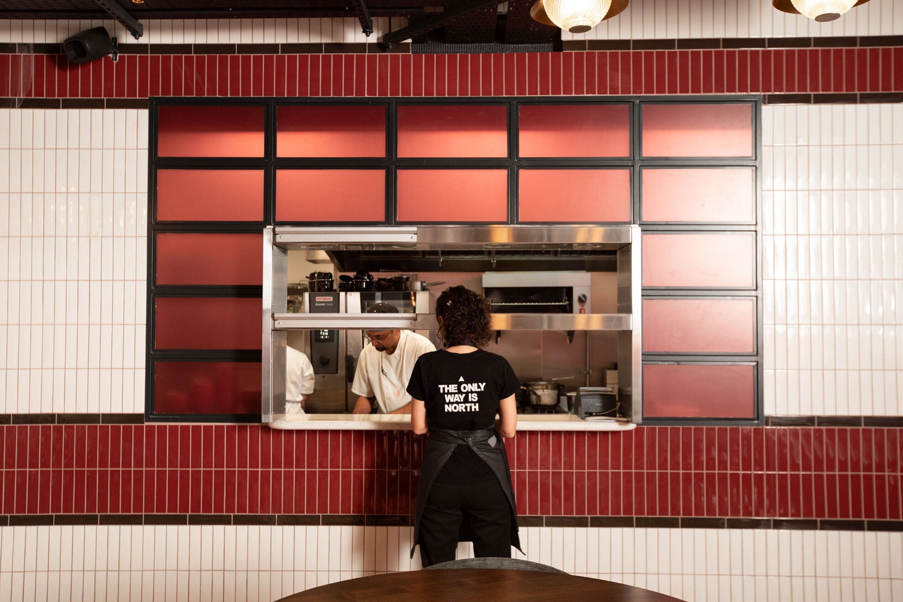 Ein Restaurantinneres mit einer Theke, rot-weiß gefliesten Wänden und einer Person, die an der Theke steht.