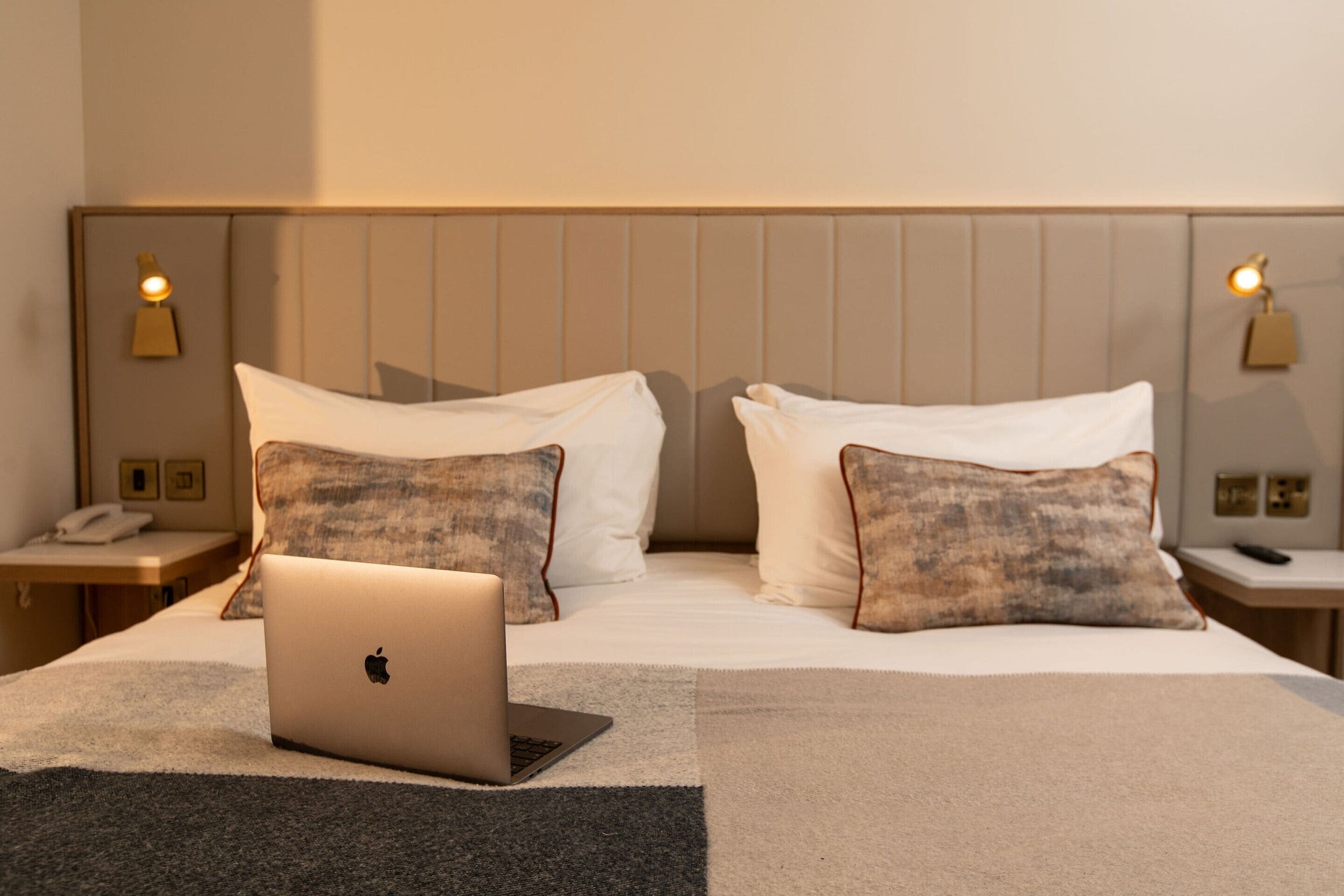 A hotel room with a bed, a laptop, and two bedside tables with lamps.