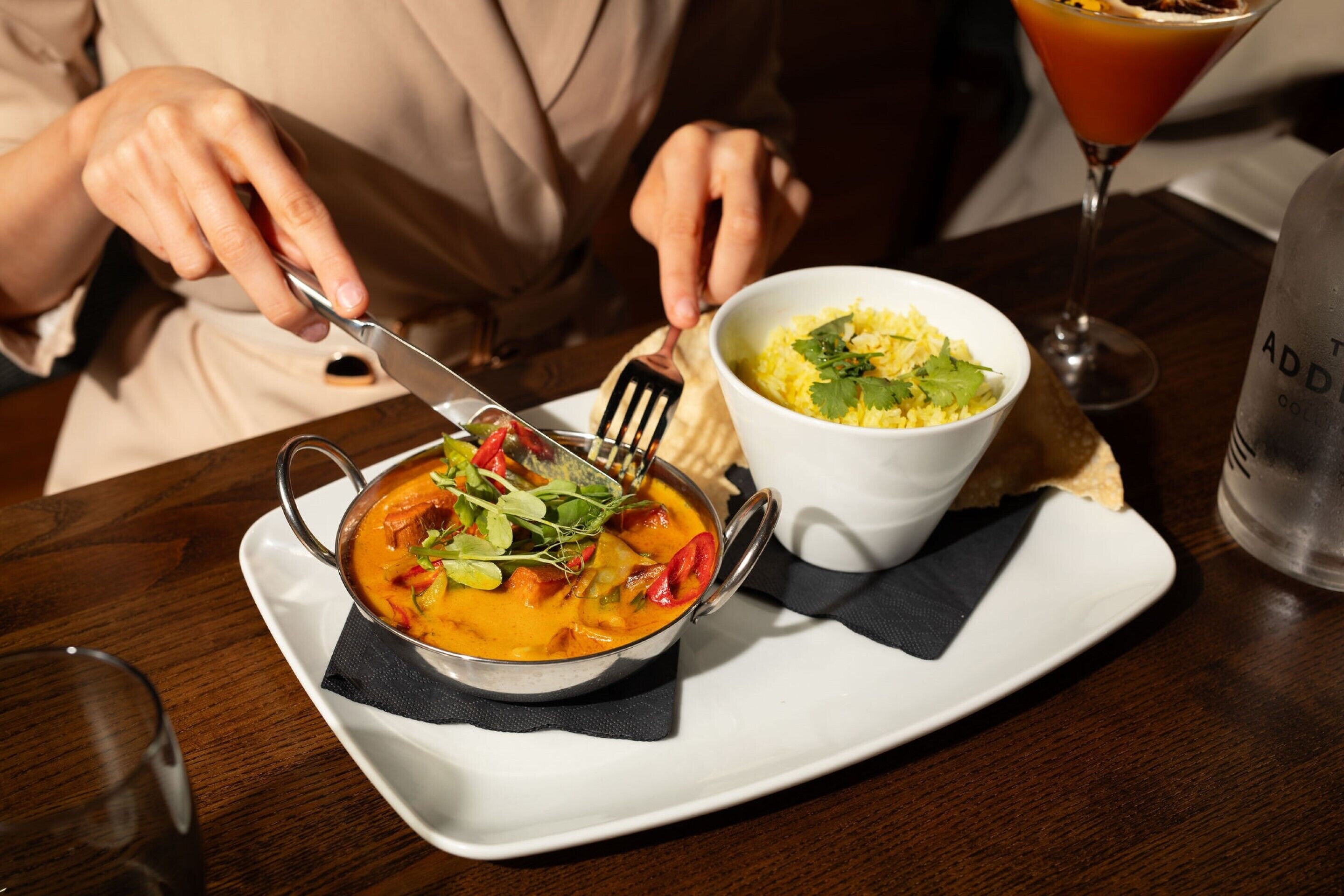 A person dining at a table with a bowl of soup, a glass of a red beverage, and a bottle of water.