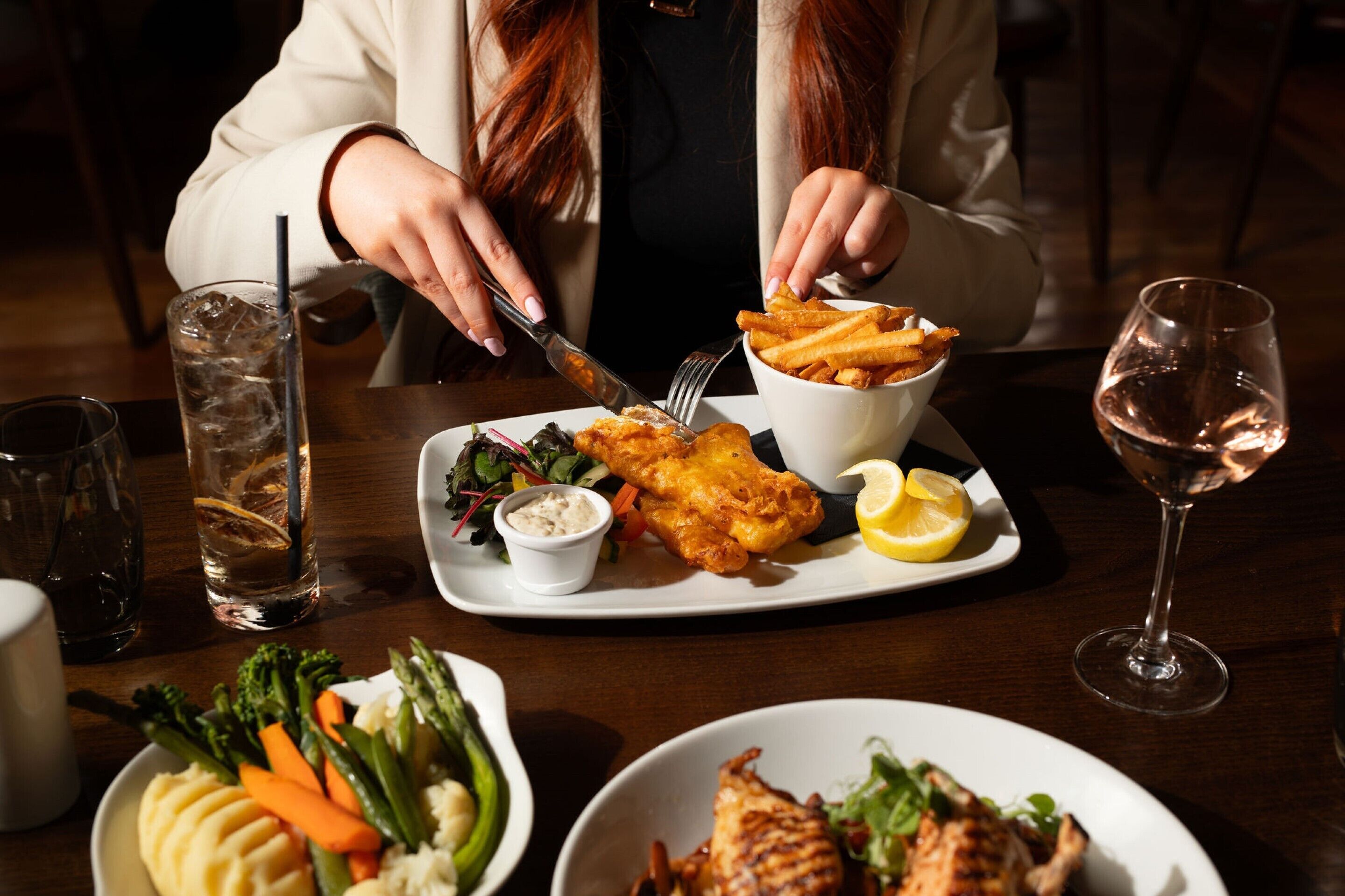 A dining table with a variety of dishes including fish and chips, salad, and grilled chicken.