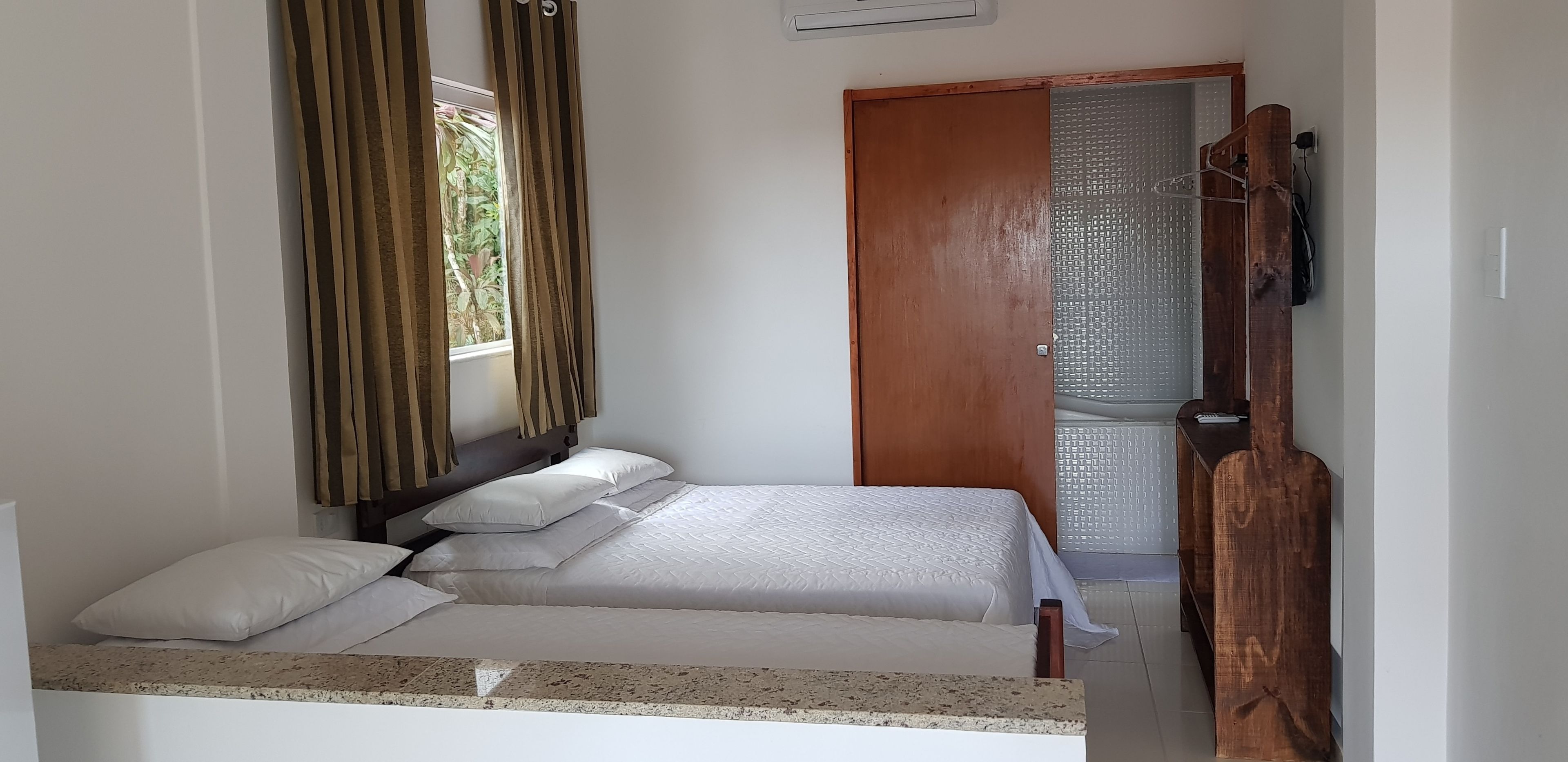 A single bed with a headboard, a wooden wardrobe, a small table, and a window with curtains.