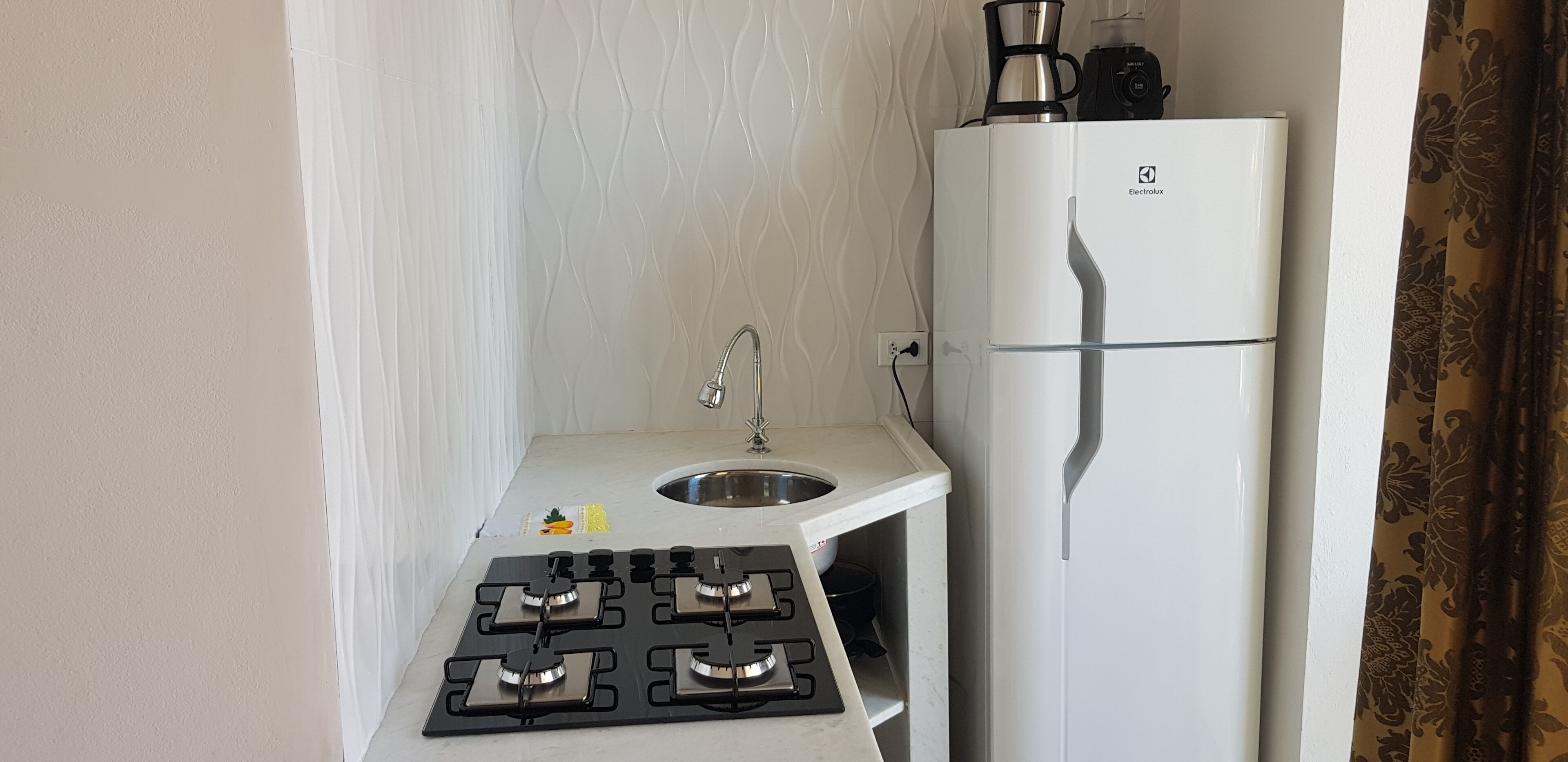 Una kitchenette compacta con estufa a gas, lavamanos y refrigerador.