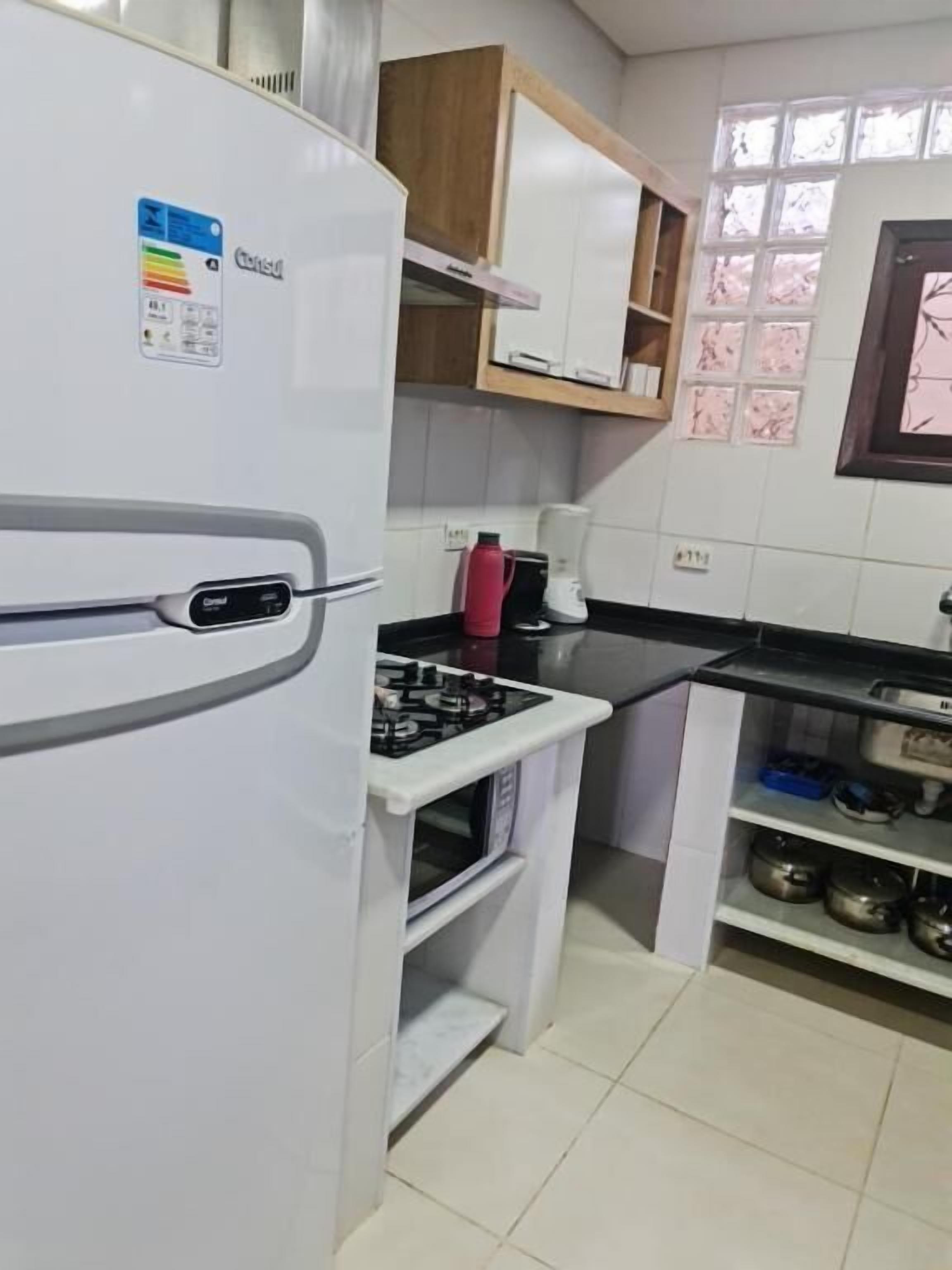 A compact kitchen with a white refrigerator, a gas stove, and a microwave. There are wooden cabinets above the counter and a window with a view of trees.
