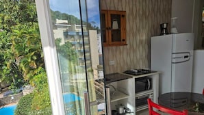 A kitchen with a view of a pool and greenery, a red chair, and a white refrigerator. - Apartamentos Casa Da Pedra (Ubatuba)